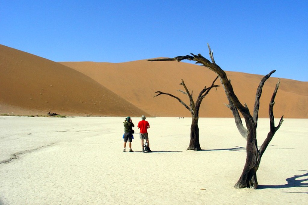 Reizigers in de Namib-woestijn bij Deadvlei, met dode bomen op de witte kleivlakte en rode duinen.