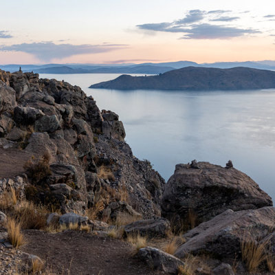 Zonsondergang bij het Titicacameer in Peru, met rotsachtige oever en eilanden op de achtergrond.