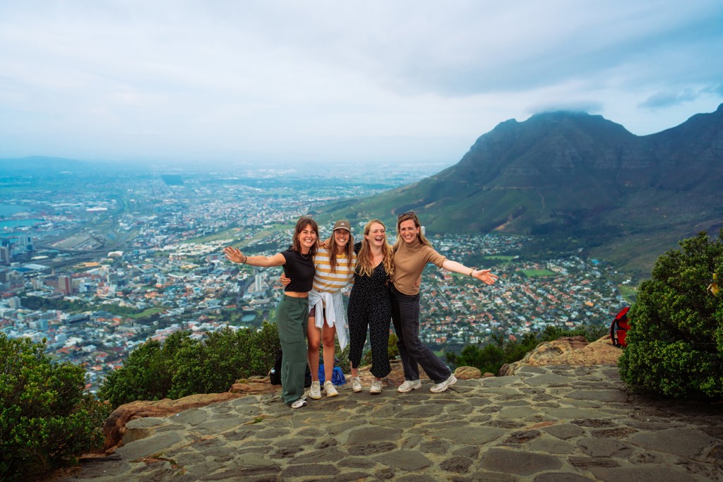Vier reizigers poseren op een uitkijkpunt met uitzicht op Kaapstad en de Tafelberg, Zuid-Afrika.