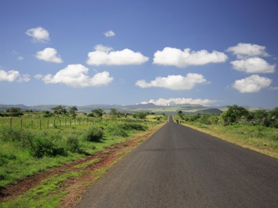 Lange weg door het groene landschap van Oost-Afrika onder een blauwe lucht met wolken.