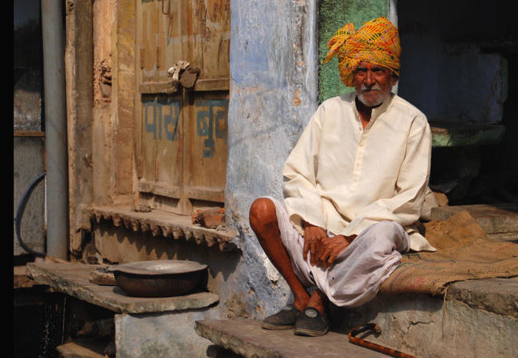 Man met kleurrijke tulband zit voor een huis in Noord-India, tijdens een groepsrondreis langs hoogtepunten.