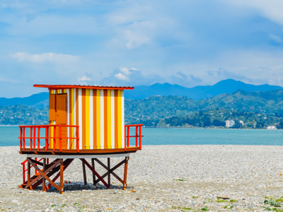 Gestreept strandwachtershuisje aan de Zwarte Zee bij Batumi, met bergen op de achtergrond in Georgië.