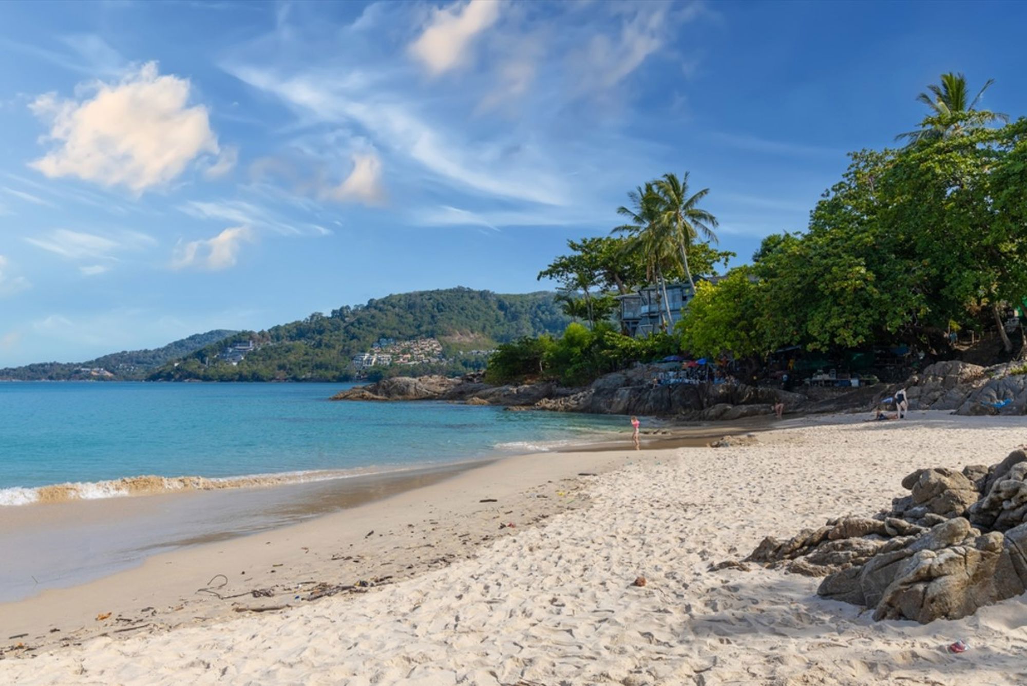 Zandstrand met palmbomen en baai met groene heuvels aan de kust van Thailand.