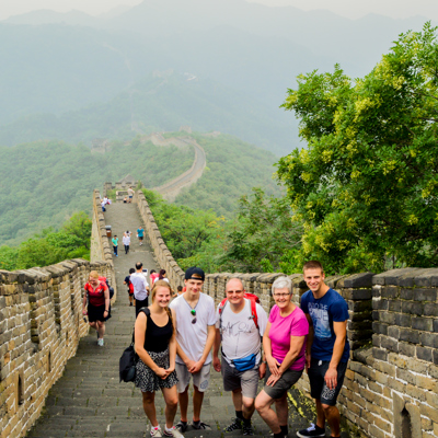 Gezin op de Chinese Muur tijdens een familiereis China, met uitzicht op groene bergen.