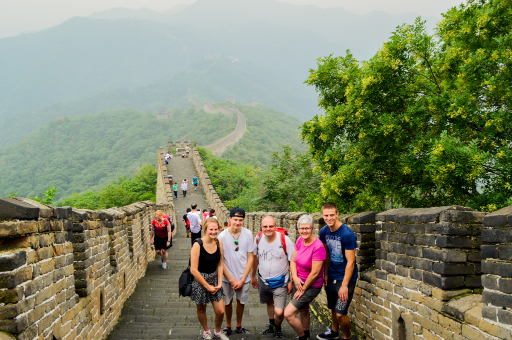 Gezin op de Chinese Muur tijdens een familiereis China, met uitzicht op groene bergen.
