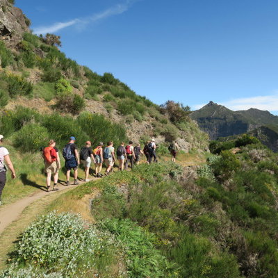 Wandelaars op bergpad met uitzicht over de groene bergen van Madeira tijdens een wandelvakantie.
