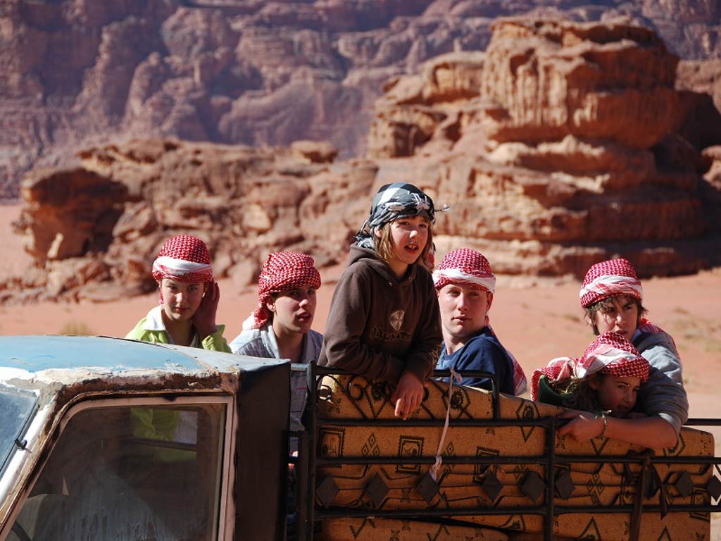 Kinderen tijdens een familiereis Jordanië in de woestijn, zittend op een pickup met rotsformaties op de achtergrond.