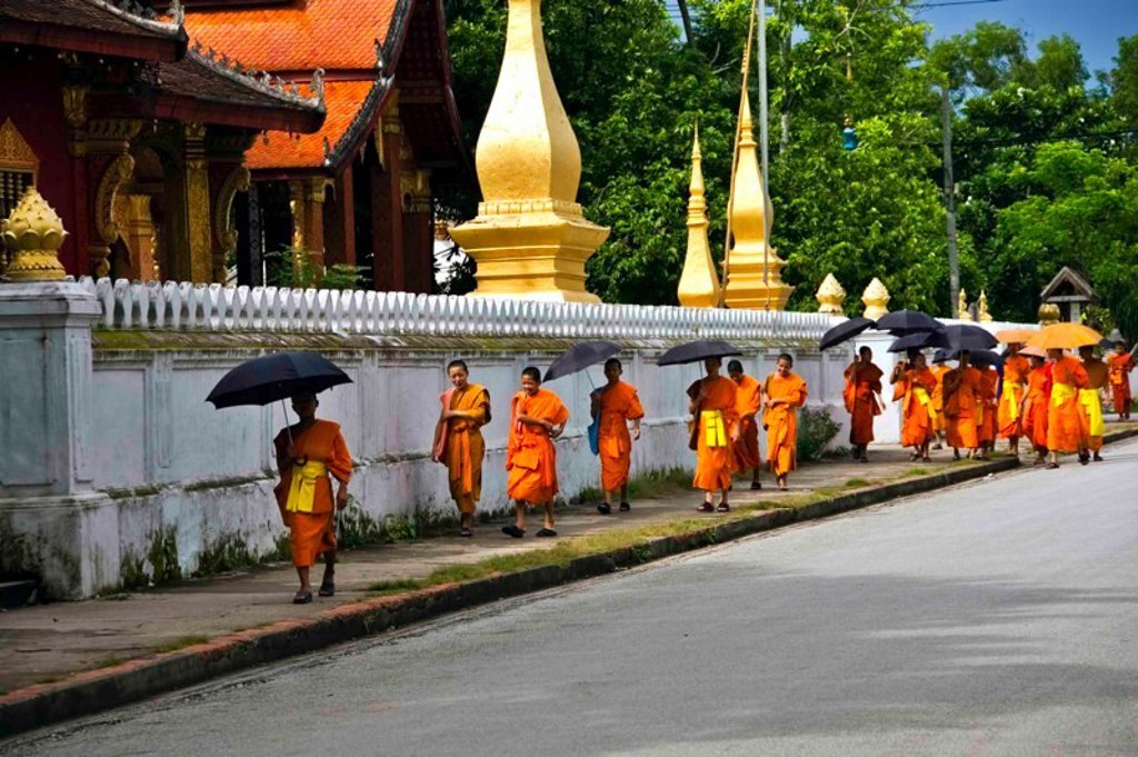 Boeddhistische monniken met parasols lopen langs een tempelmuur in Laos tijdens familiereis Thailand, Laos en Cambodja.