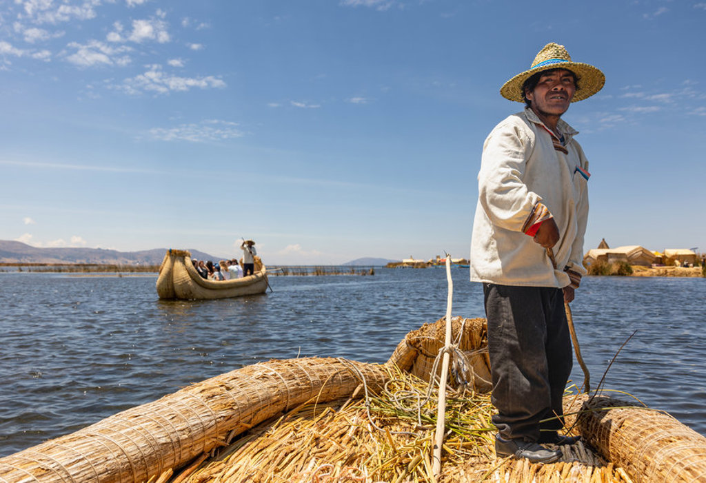 Bootman op een rieten boot op het Titicacameer, Peru, met toeristen op de achtergrond.