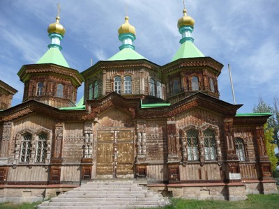 Houten orthodoxe kerk met drie groene koepels en gouden kruisen in Kirgistan.