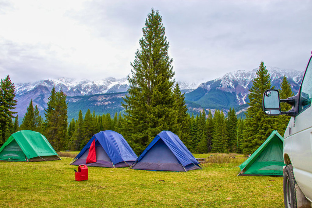 Kampeerplek met tenten in de Canadese Rockies, omringd door dennenbos en besneeuwde bergtoppen.