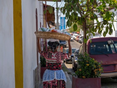 Straatbeeld in Guatemala met vrouw in traditionele kleding die een mand met goederen op haar hoofd draagt.