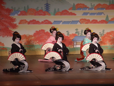 Traditionele Japanse dansvoorstelling met danseressen in kimono en waaiers op een podium.