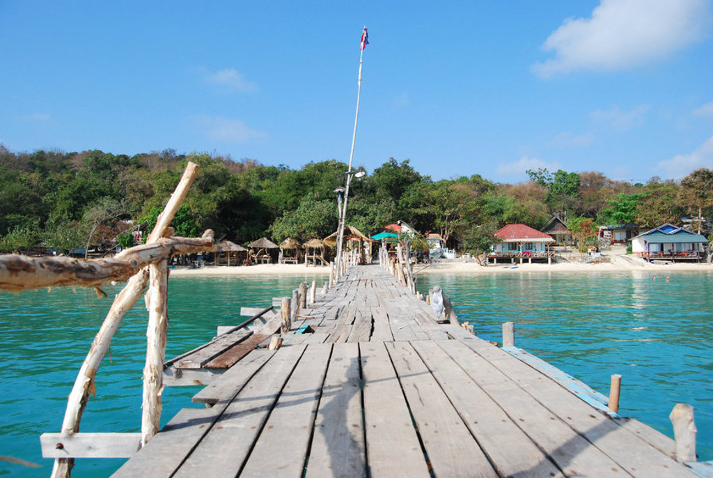 Houten pier naar een strand met bungalows en groene heuvels in Thailand, tijdens de Familiereis Thailand Hoogtepunten.