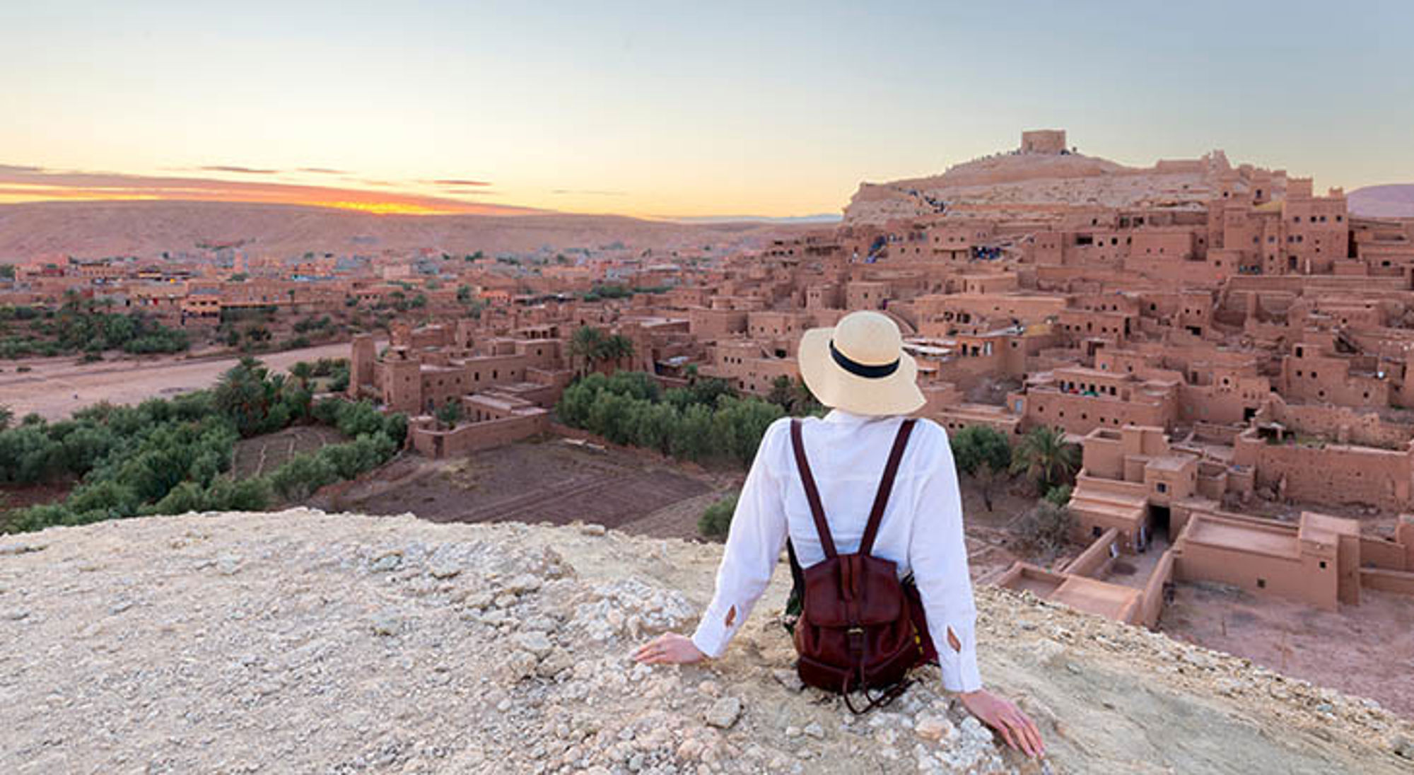 Reiziger kijkt uit over de kasbah van Aït Ben Haddou bij zonsondergang in Marokko.