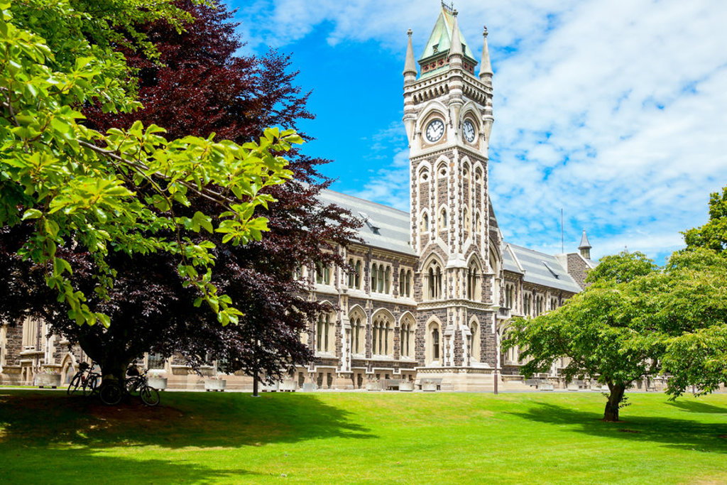 Historisch universiteitsgebouw met klokkentoren in Dunedin, Nieuw-Zeeland, omringd door groen.