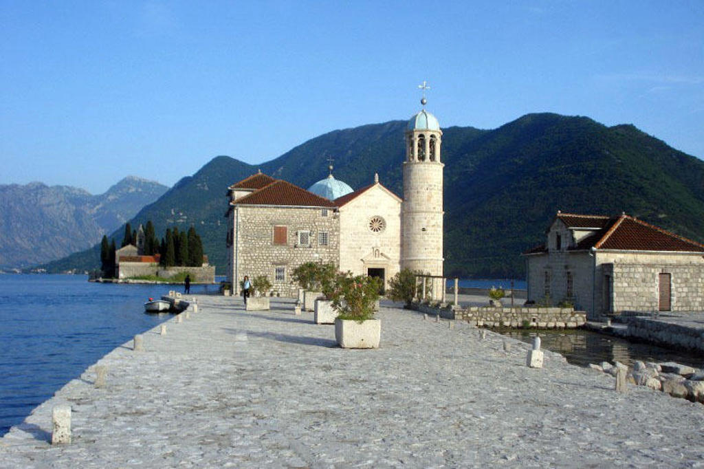 Kerk op eilandje in de Baai van Kotor, Montenegro, met bergen op de achtergrond.