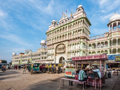 Gevel van de kleurrijke Ram Mandir-tempel in Jaipur, met riksja’s en eetkraampjes op straat.