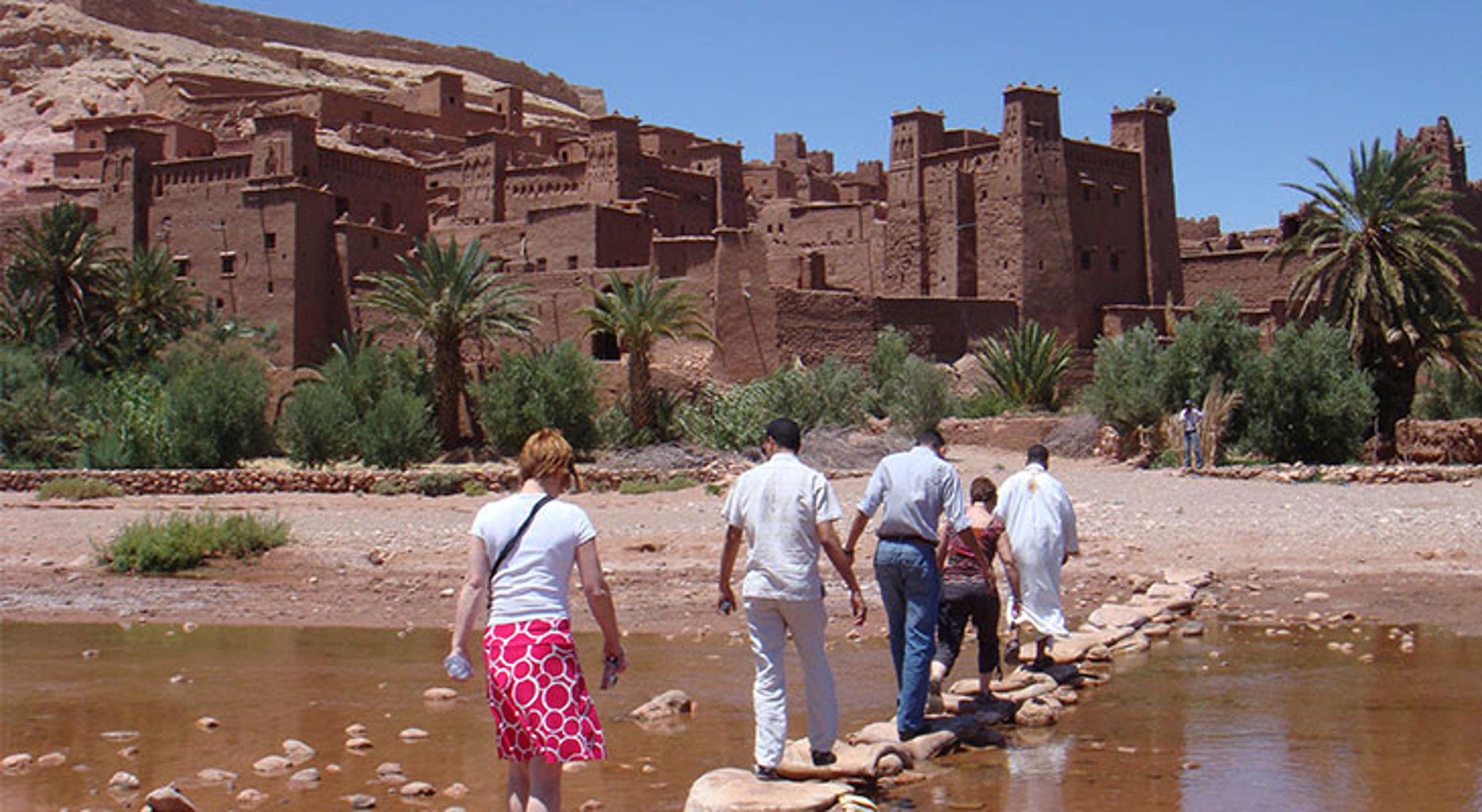 Toeristen steken een rivier over naar de kasbah van Aït Ben Haddou in Marokko.