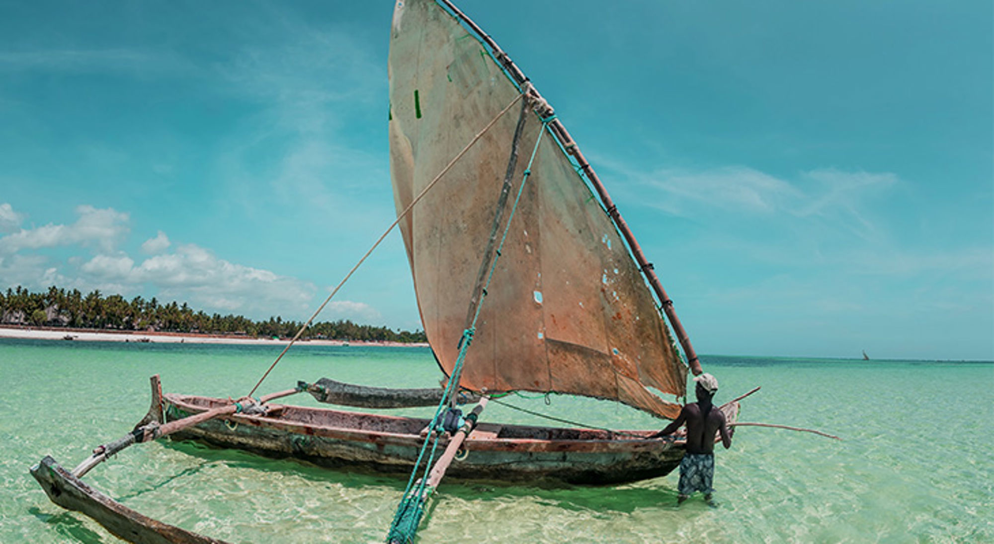Traditionele dhow-zeilboot in ondiep turquoise water bij een tropisch strand in Kenia.