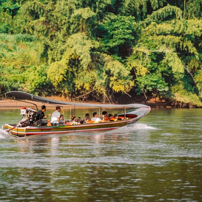 Longtailboot met reizigers op een rivier in Thailand, langs groene jungle tijdens een familiereis.