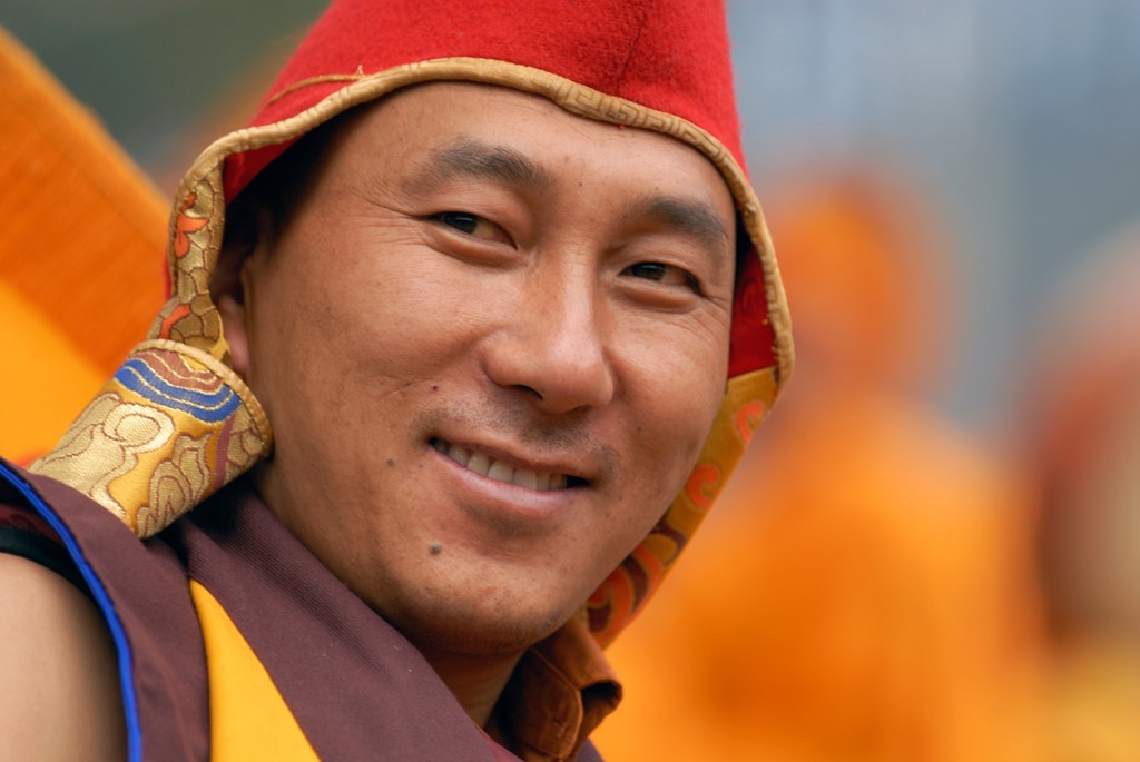 Portret van een boeddhistische monnik in Sikkim of Bhutan, met rode muts en traditionele kleding.