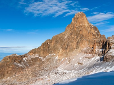 Rotsachtige bergtop met sneeuwresten onder een blauwe lucht in Kenia.