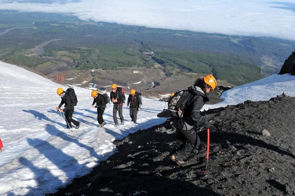 Groep wandelaars met helmen klimt over sneeuw en vulkanisch gesteente tijdens groepsrondreis Patagonië en Paaseiland.