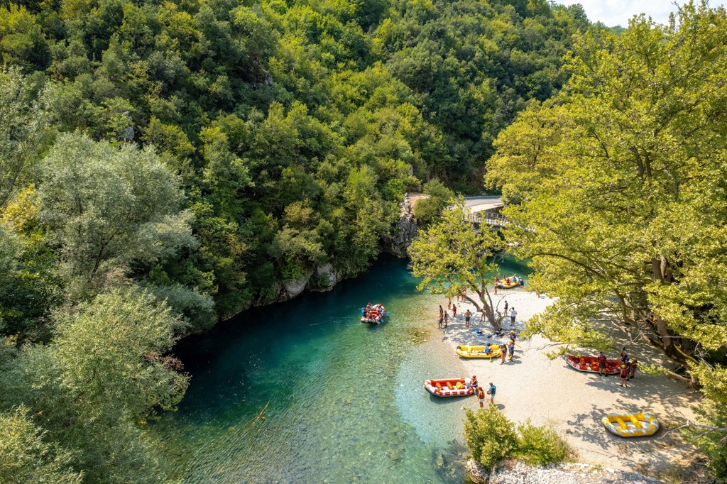 Raften op een helderblauwe rivier met strandje in het groen, tijdens een familiereis Noord-Griekenland.