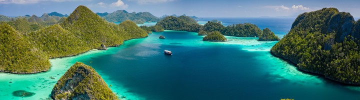 Panorama van de kalkstenen eilanden en turquoise lagunes van Raja Ampat, Indonesië, met een boot op zee.