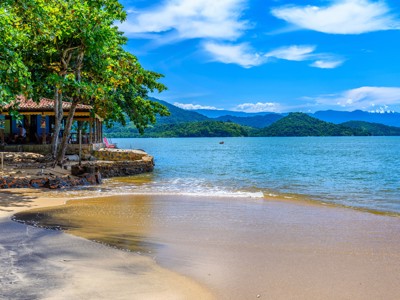 Strand aan een baai bij Paraty, met groen begroeide heuvels en helderblauwe lucht, tijdens route Brazilië en Buenos Aires.