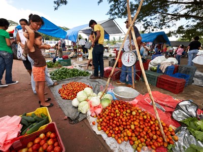 Lokale groentemarkt in Guatemala met tomaten, kool en paprika’s op zeilen en een weegschaal.