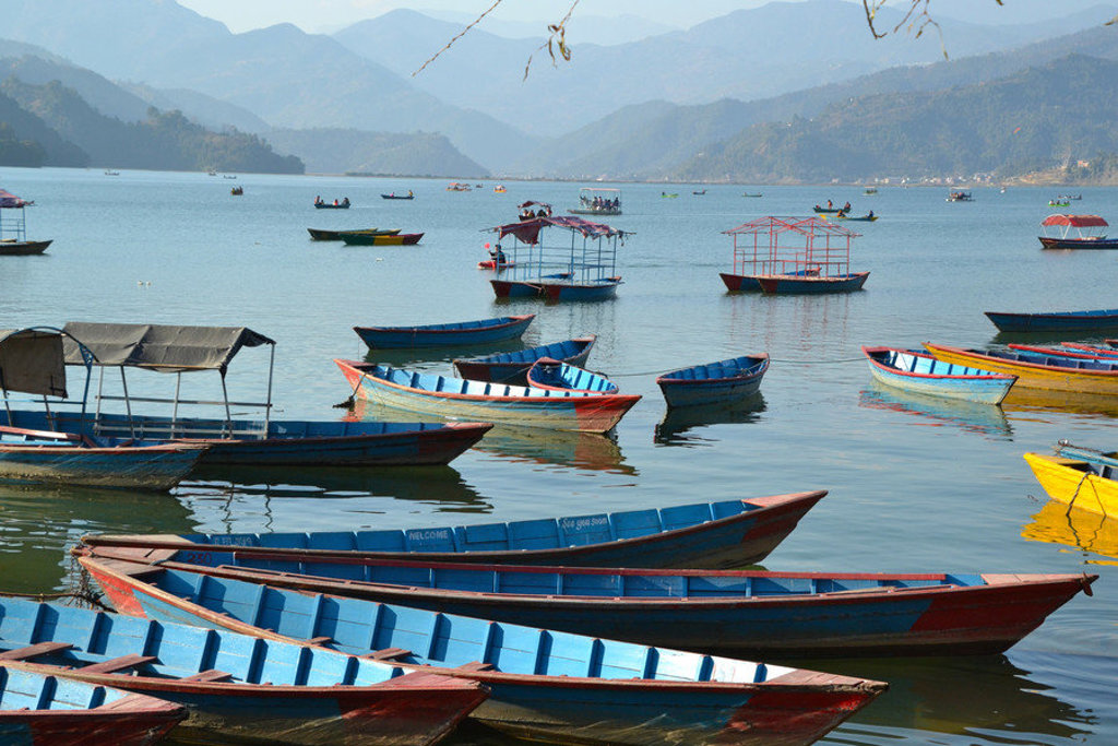 Kleurrijke roeiboten op het Phewa-meer bij Pokhara, Nepal, met bergen op de achtergrond.