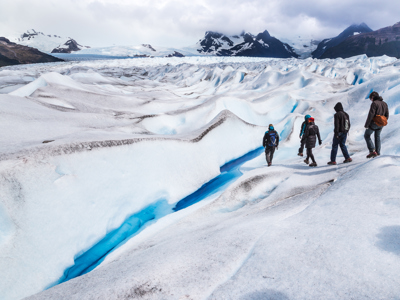 Wandelaars met stijgijzers op een gletsjer in Patagonië, met blauwe ijsspleet en besneeuwde bergen op de achtergrond.