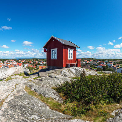 Rood houten huisje op rotsen met uitzicht over een kustplaats in Zweden tijdens een groepsrondreis Scandinavië.