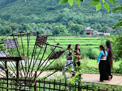 Vrouwen lopen langs rijstvelden en een traditioneel waterrad in het groene platteland van Vietnam.